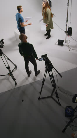 Vertical-Video-Overhead-Shot-Of-Actors-Rehearsing-Movie-Or-Video-Scene-In-Studio-With-Film-Camera-And-Lighting-Crew